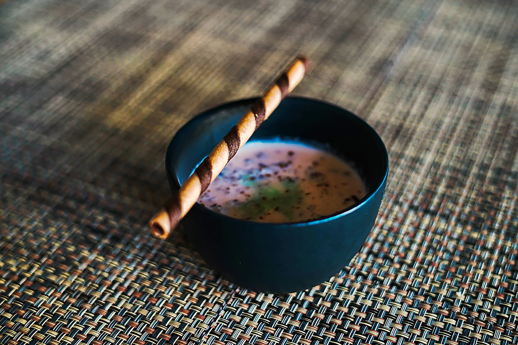 Crema fría de melón con Midori y tierra de vainilla en un plato hondo y una varita de chocolate de especialidad Delli de hotel Sunset Palace Mazatlán