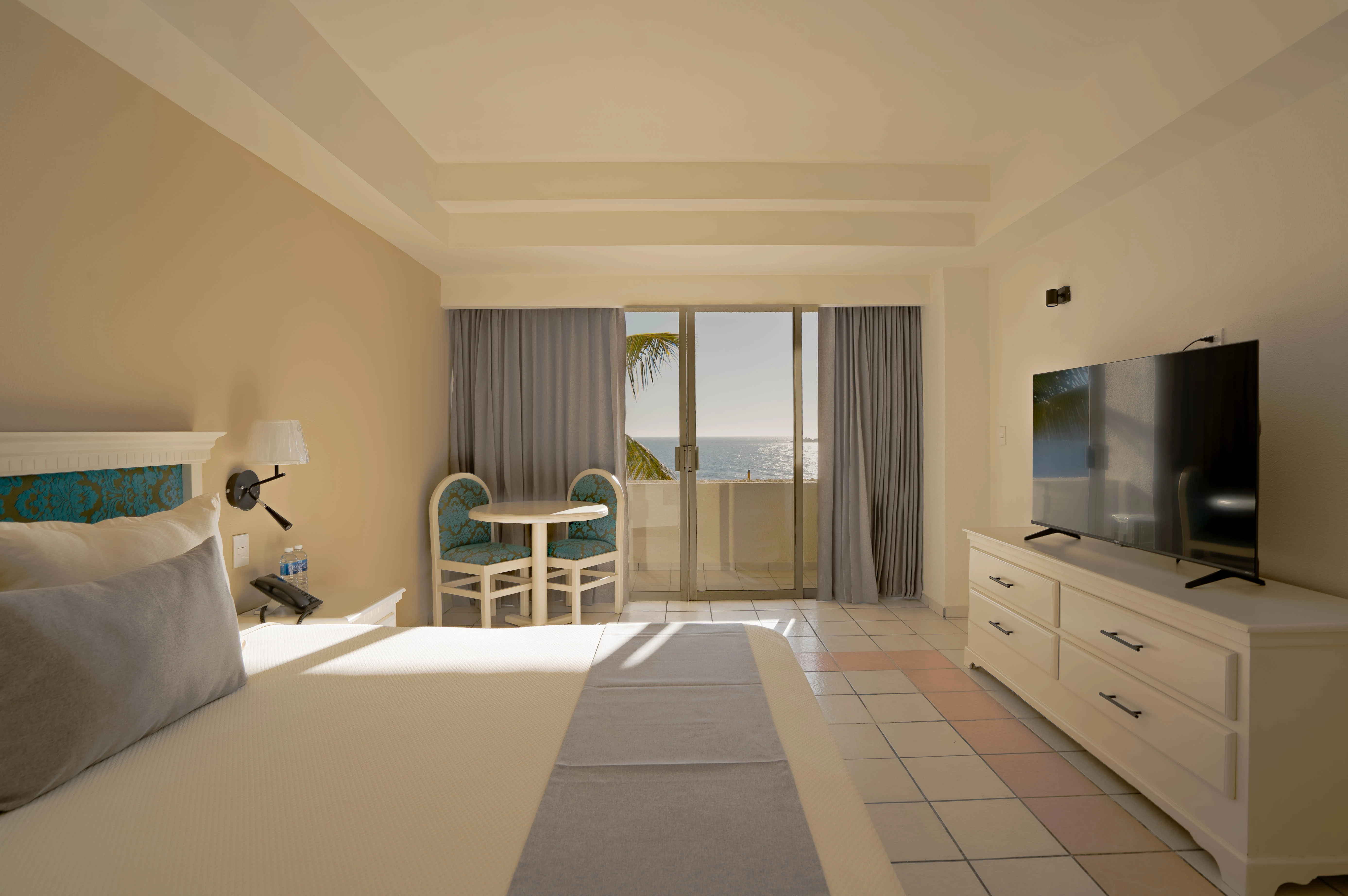 habitación standard con balcón y vista al mar, cama kingsize, mesa con dos sillas del hotel sunset palace Mazatlán